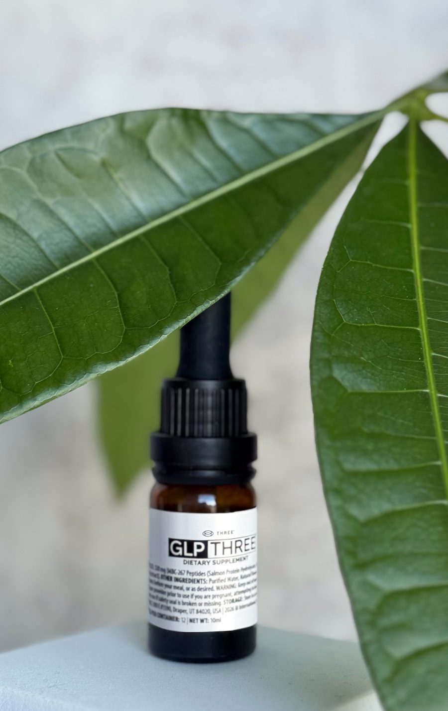 GLP-THREE bottle beside a green leaf