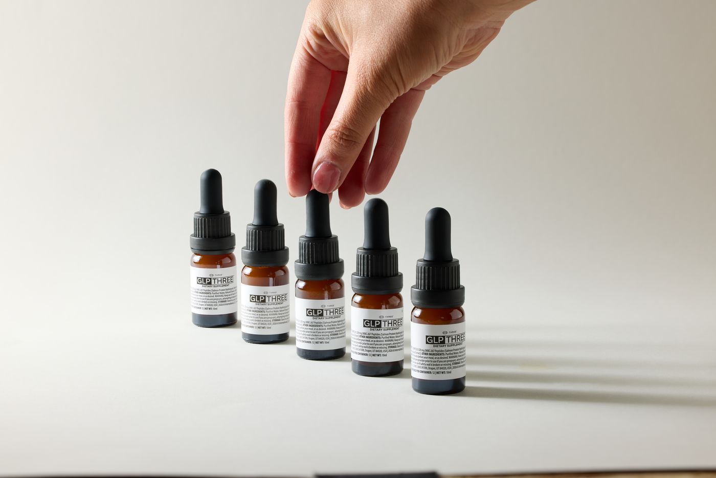 A hand picking one GLP-THREE bottle from a row of five