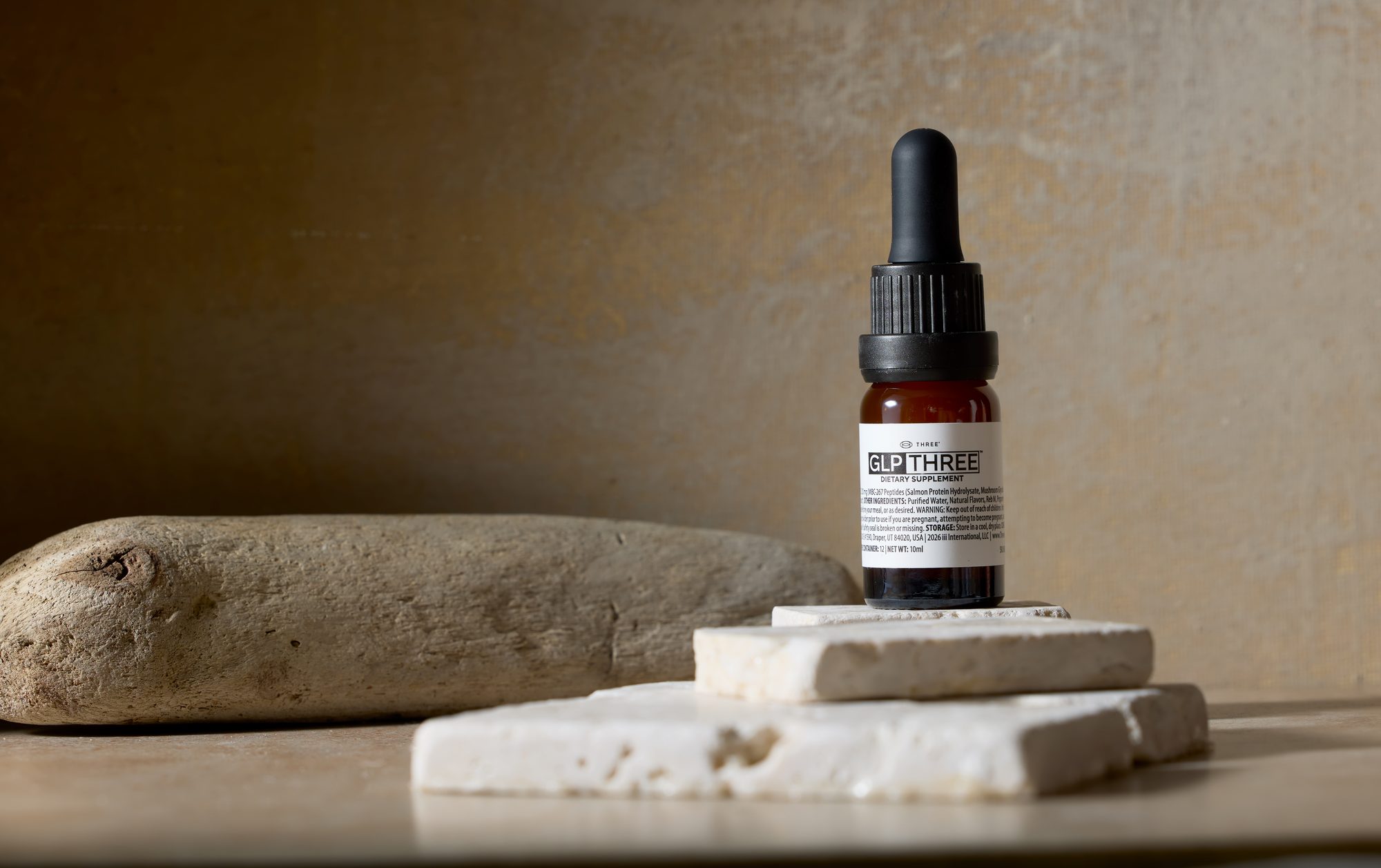GLP-THREE dropper bottle on travertine stone beside driftwood
