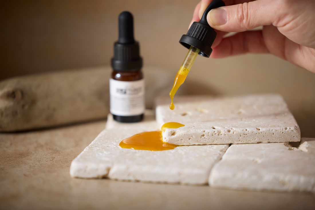 Golden GLP-THREE drops falling from the dropper onto travertine stone